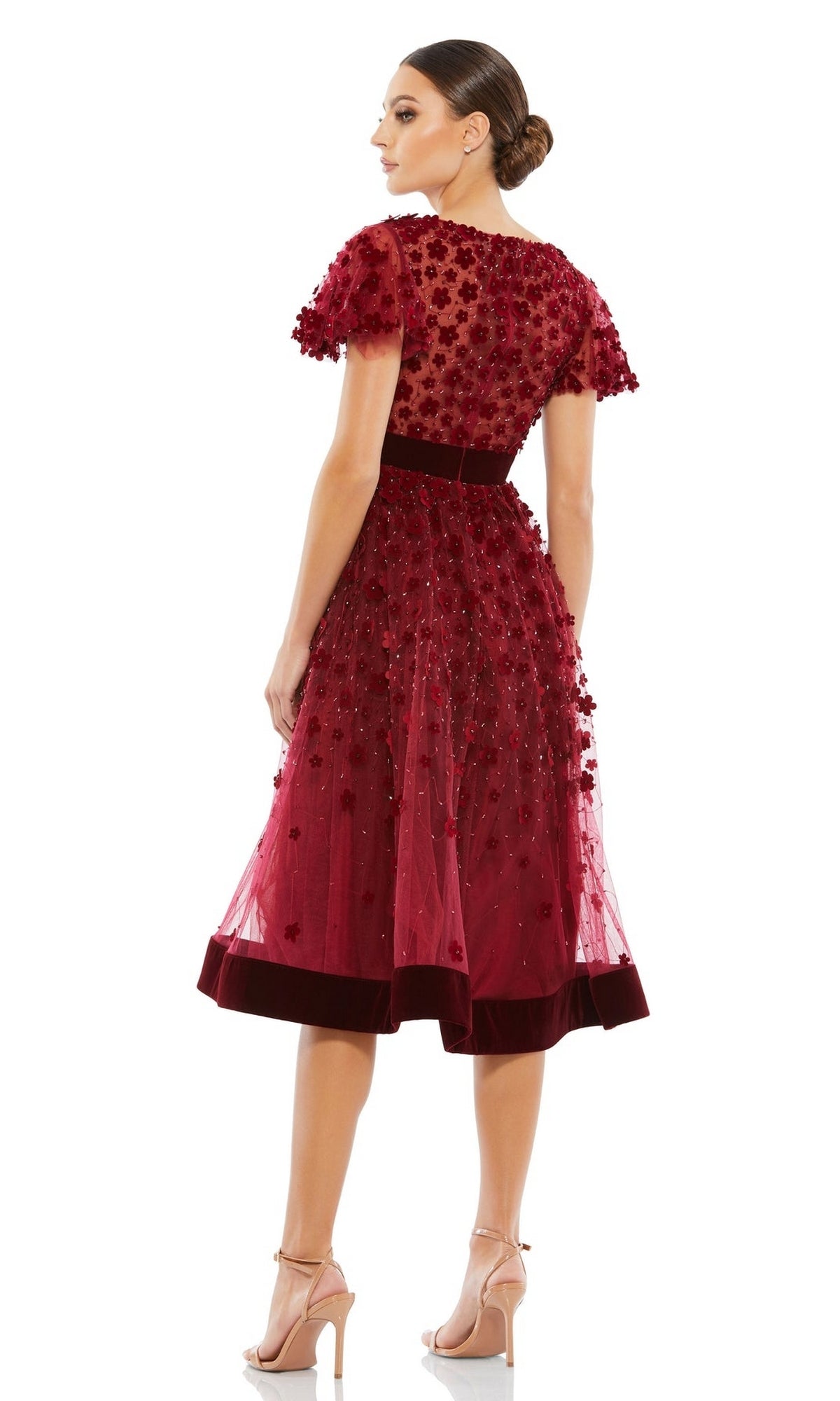 Woman wearing the Mac Duggal 67854 Floral Midi Wedding Guest Dress—a knee-length, short-sleeve dress with floral embellishments, sheer overlay, and velvet trim—stands in heels against a white background for a vintage look.